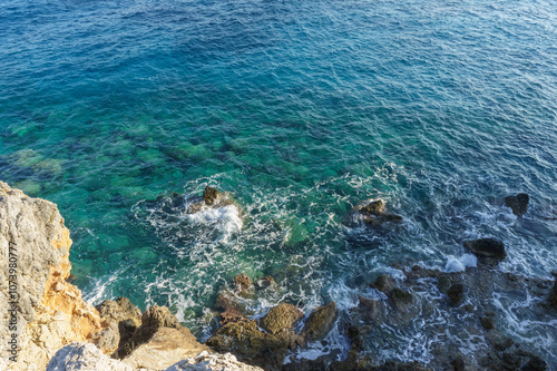 Calm ocean waves gently lap against rocky shores beneath a clear blue sky at midday. photo