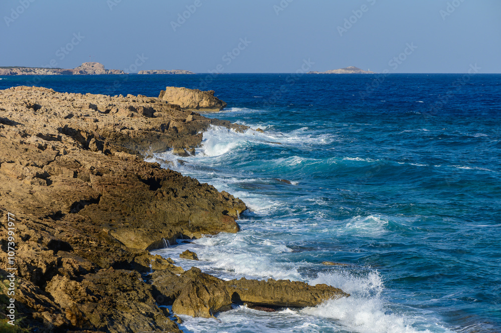 Waves crashing against rocky shores at a serene coastal location under a bright blue sky. Waves crashing against rocky shores at a serene coastal location under a bright blue sky.