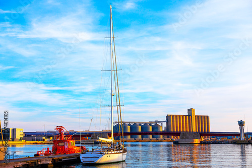 Boats moored in the port of Tarragona, Spain. Sailboat is moored at a dock alongside a vibrant red boat