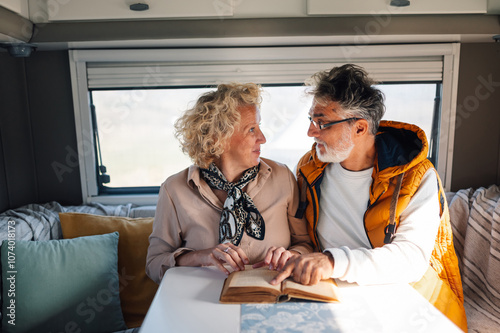 Senior couple reading book inside camper van during road trip