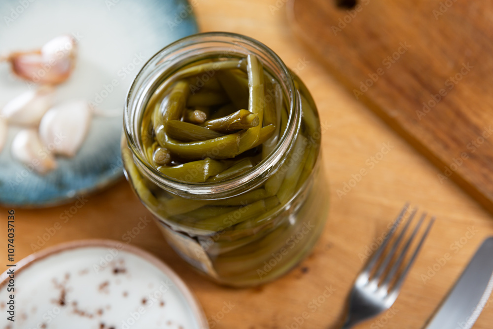There is open jar with pickled green young ramson shoots on table. Mediterranean European vegetable snack There is open jar with pickled green young ramson shoots on table. Mediterranean European vegetable snack
