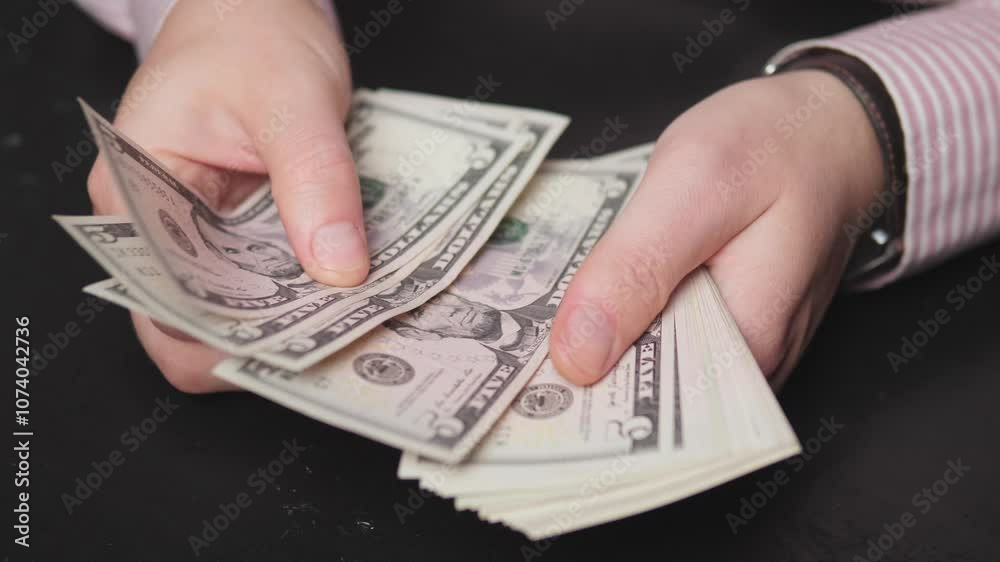 hands are carefully counting multiple stacks of US dollar bills placed on a dark surface hands are carefully counting multiple stacks of US dollar bills placed on a dark surface
