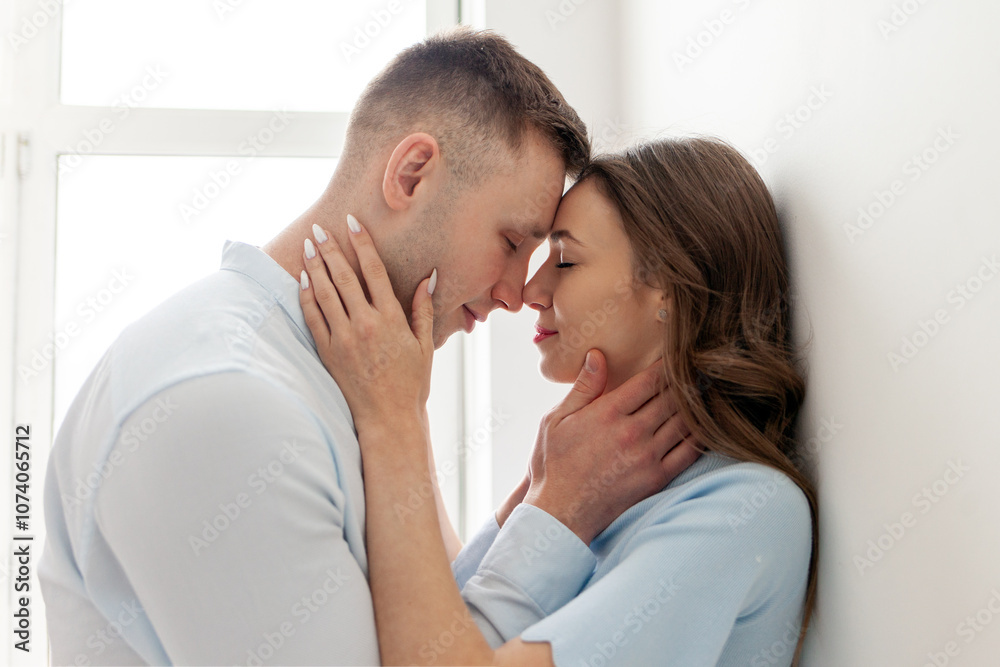 young couple in love stands close, holds the neck and looks into the eyes before kissing, the man passionately kisses the woman at home and smiles, close-up young couple in love stands close, holds the neck and looks into the eyes before kissing, the man passionately kisses the woman at home and smiles, close-up