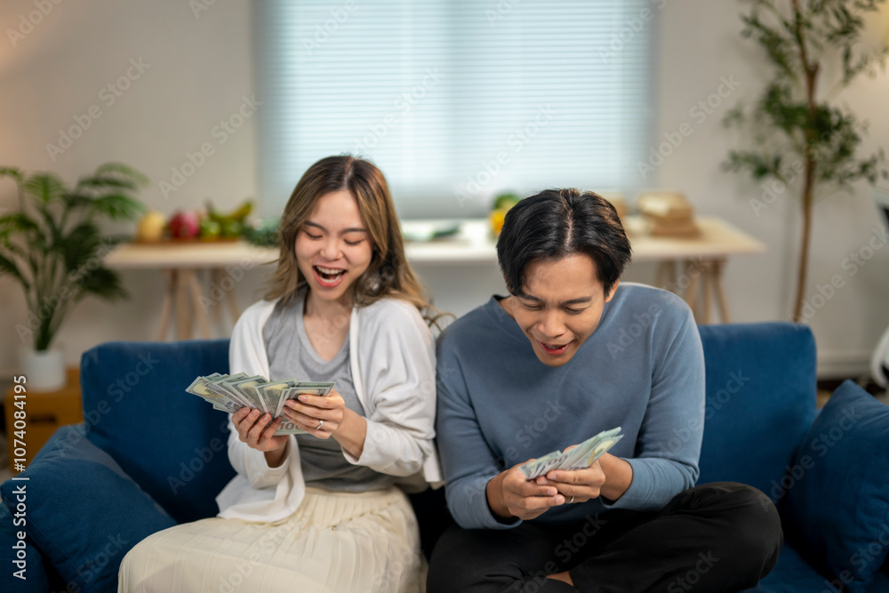 A man and a woman are sitting on a blue couch, both holding money A man and a woman are sitting on a blue couch, both holding money