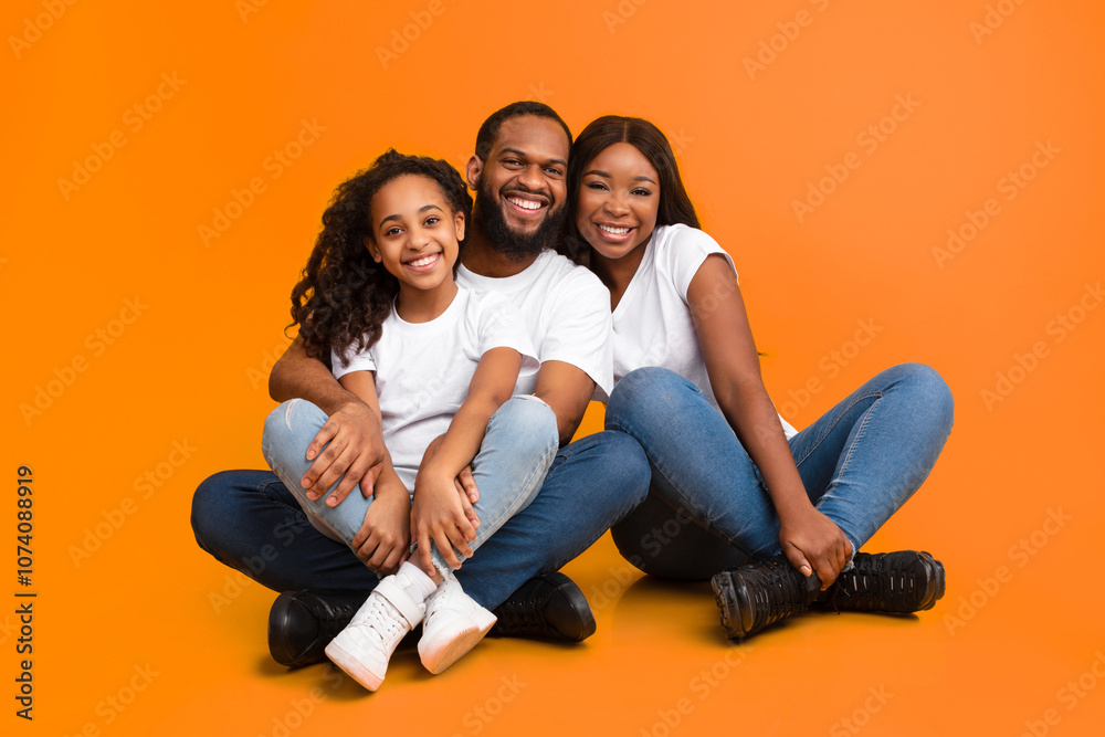 Happy Loving Family. Portrait of African American man, woman and girl sitting on the floor isolated on yellow orange wall. Smiling couple posing with daughter looking at camera. Togetherness, Bonding Happy Loving Family. Portrait of African American man, woman and girl sitting on the floor isolated on yellow orange wall. Smiling couple posing with daughter looking at camera. Togetherness, Bonding