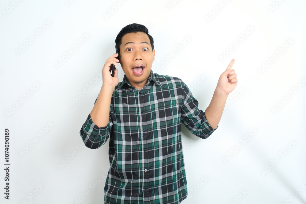 Fototapeta premium surprised asian man pointing hand while talking on smartphone isolated on white background, male wear casual green shirt
