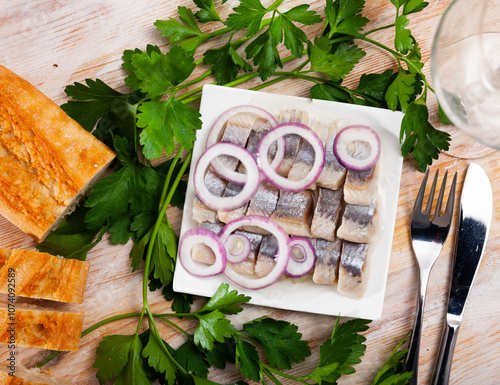 Fototapeta Naklejka Na Ścianę i Meble -  Plate with slices of salted fillet of herring with onion on wooden table with fresh parsley