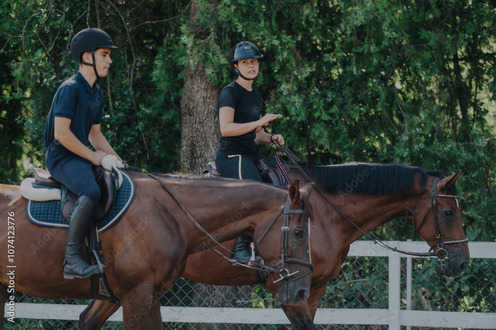 Two young riders are being instructed on horseback riding in a serene outdoor environment, surrounded by lush greenery. The image captures the focus and training in a natural equestrian setting. Two young riders are being instructed on horseback riding in a serene outdoor environment, surrounded by lush greenery. The image captures the focus and training in a natural equestrian setting.