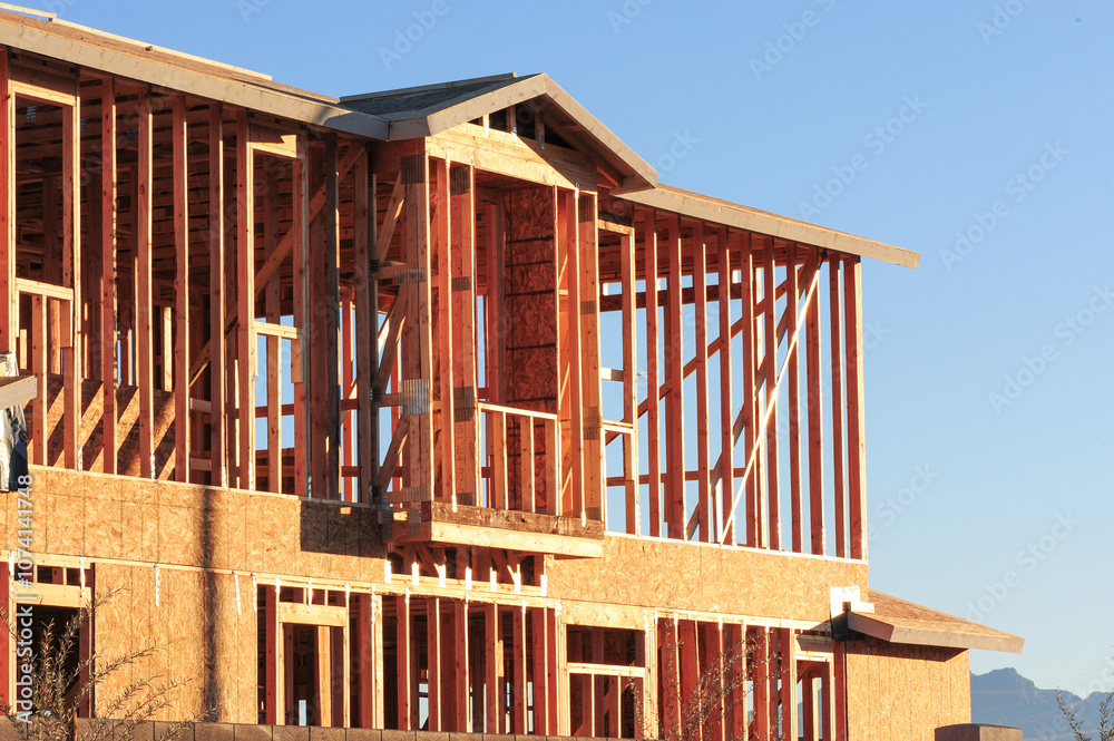 Obraz premium Exterior view of wood framing and structural components on a two-story house under construction, illustrating early-phase residential building with exposed studs, sheathing, and architectural design