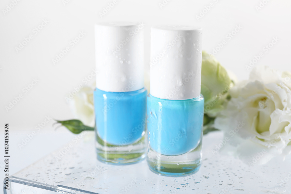 Nail polishes in bottles and beautiful flowers on light background, closeup