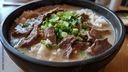 A bowl of seolleongtang, milky beef bone soup with slices of beef, rice, and green onions.