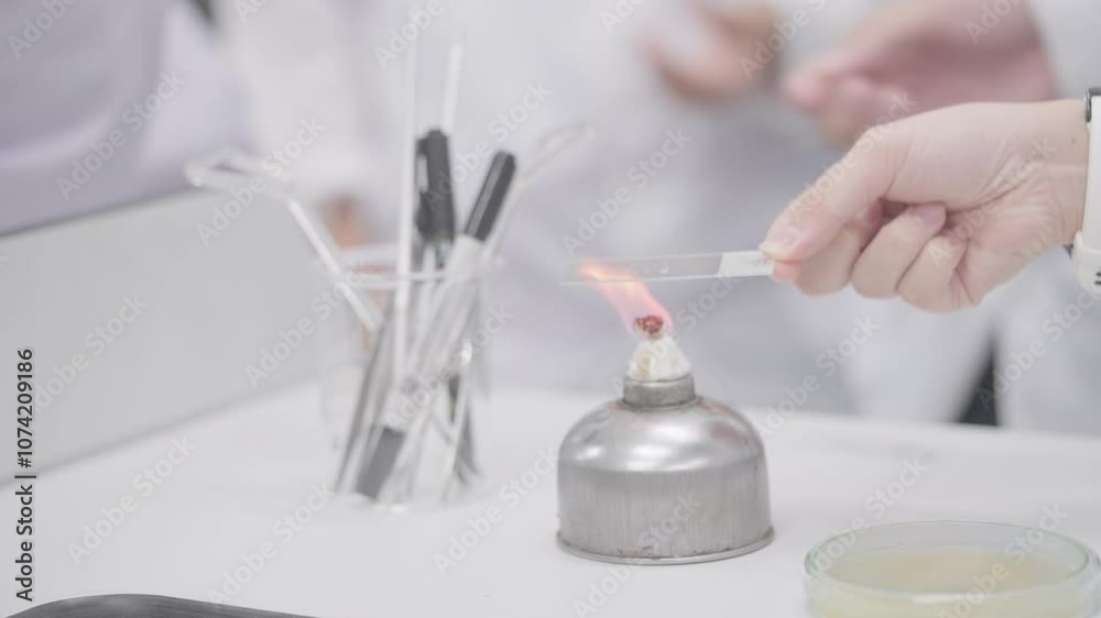 A person is holding a lighter near a small container. The container is on a table and has a white label on it. The person is wearing a white lab coat A person is holding a lighter near a small container. The container is on a table and has a white label on it. The person is wearing a white lab coat