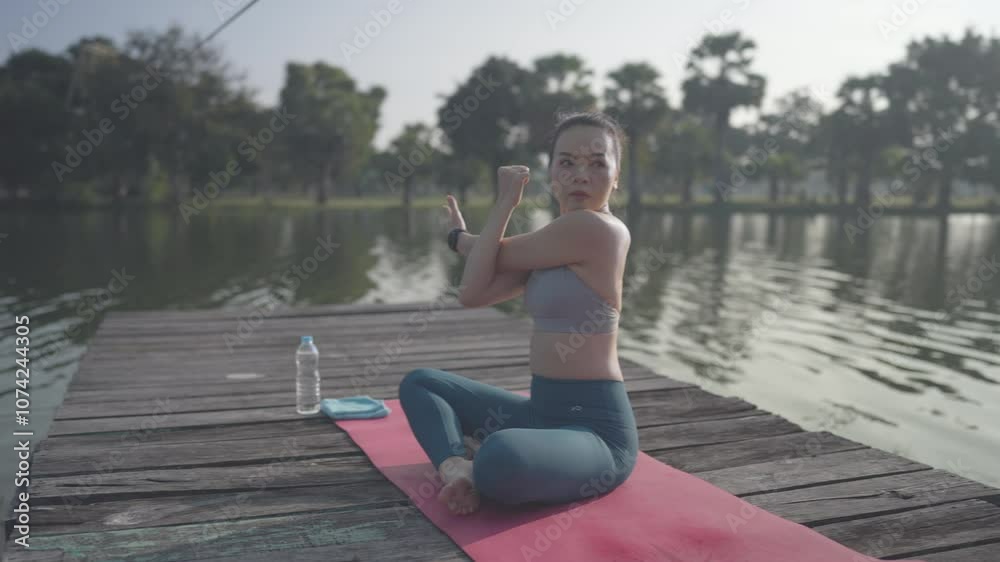 A woman is sitting on a yoga mat on a dock by a body of water. She is holding her hands together and she is in a meditative state A woman is sitting on a yoga mat on a dock by a body of water. She is holding her hands together and she is in a meditative state