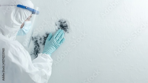 A person in protective gear cleaning mold from a wall.