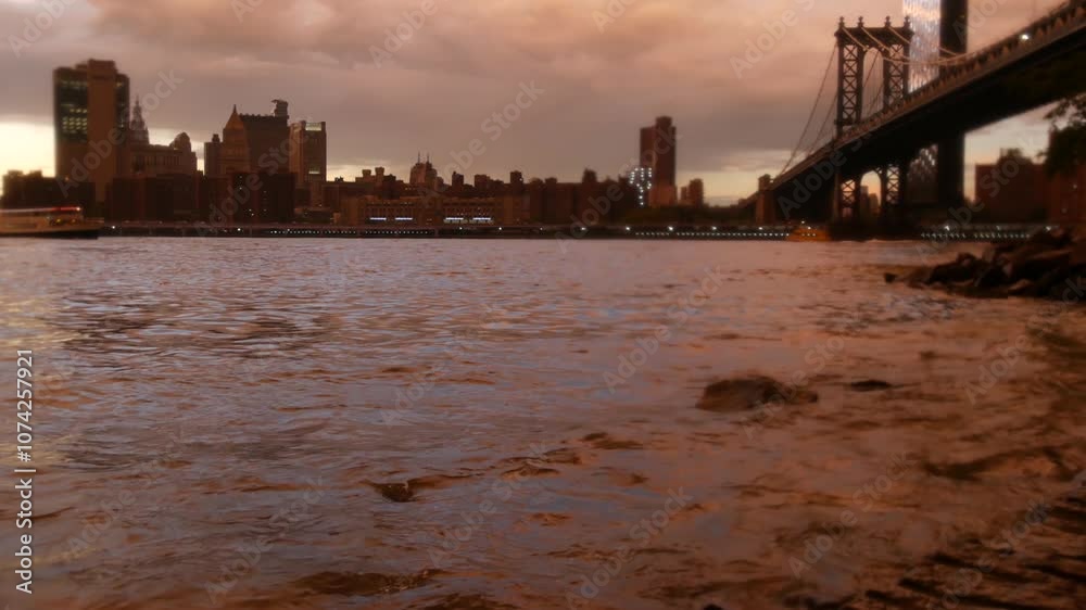 Rainy New York City under Manhattan Bridge in Brooklyn. Pink sunset after rain by river water on waterfront Dumbo promenade, East River. Foggy day weather on riverfront below bridge. Evening twilight. Rainy New York City under Manhattan Bridge in Brooklyn. Pink sunset after rain by river water on waterfront Dumbo promenade, East River. Foggy day weather on riverfront below bridge. Evening twilight.