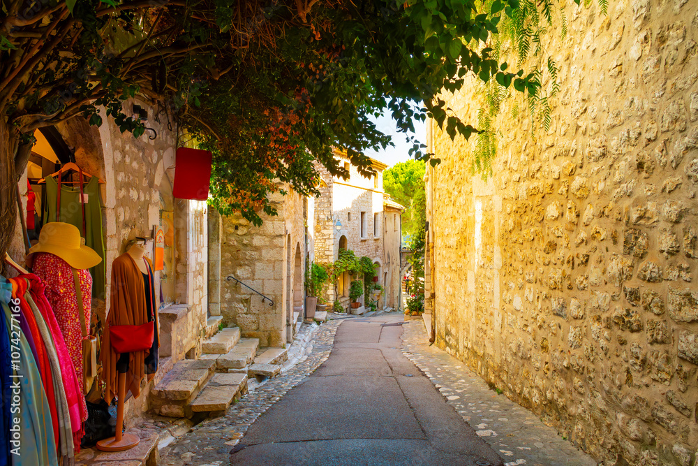 Obraz premium A narrow shady cobblestone alley with shops and boutiques in the hilltop medieval village of Saint-Paul de Vence, France, in the Provence region of Southern France.