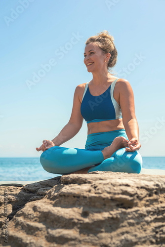 Yoga woman sitting in lotus position namaste hands cliff rock beach sea blue sky