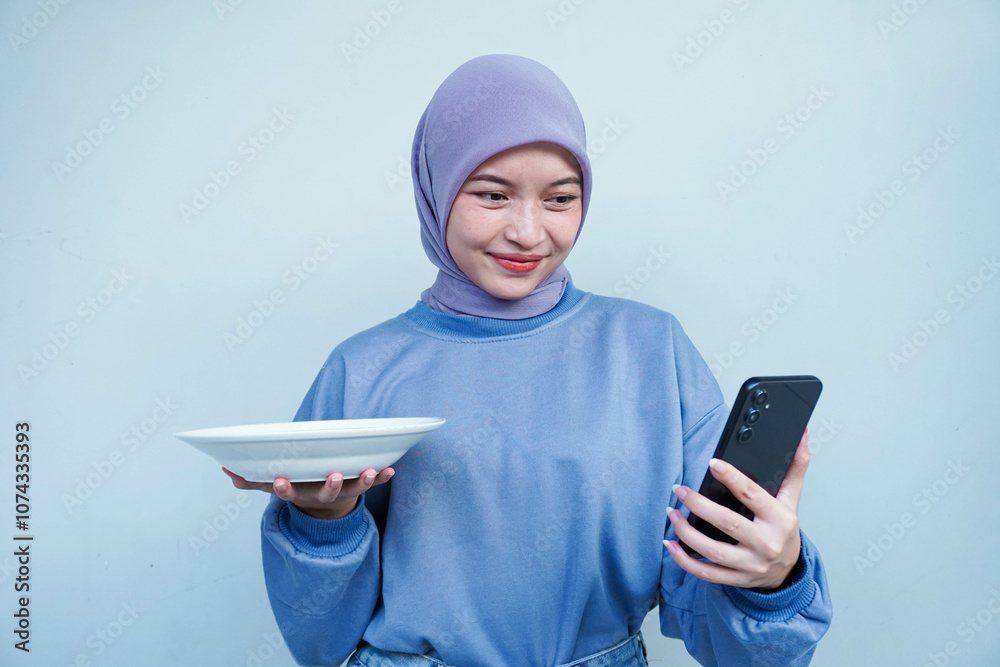 Happiness Asian Muslim woman is fasting and hungry and holding cutlery while looking phone get idea about what to eat. Online food concept. Happiness Asian Muslim woman is fasting and hungry and holding cutlery while looking phone get idea about what to eat. Online food concept.