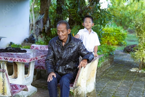 An old man sitting at a stone table With a grandchild giving a back massage