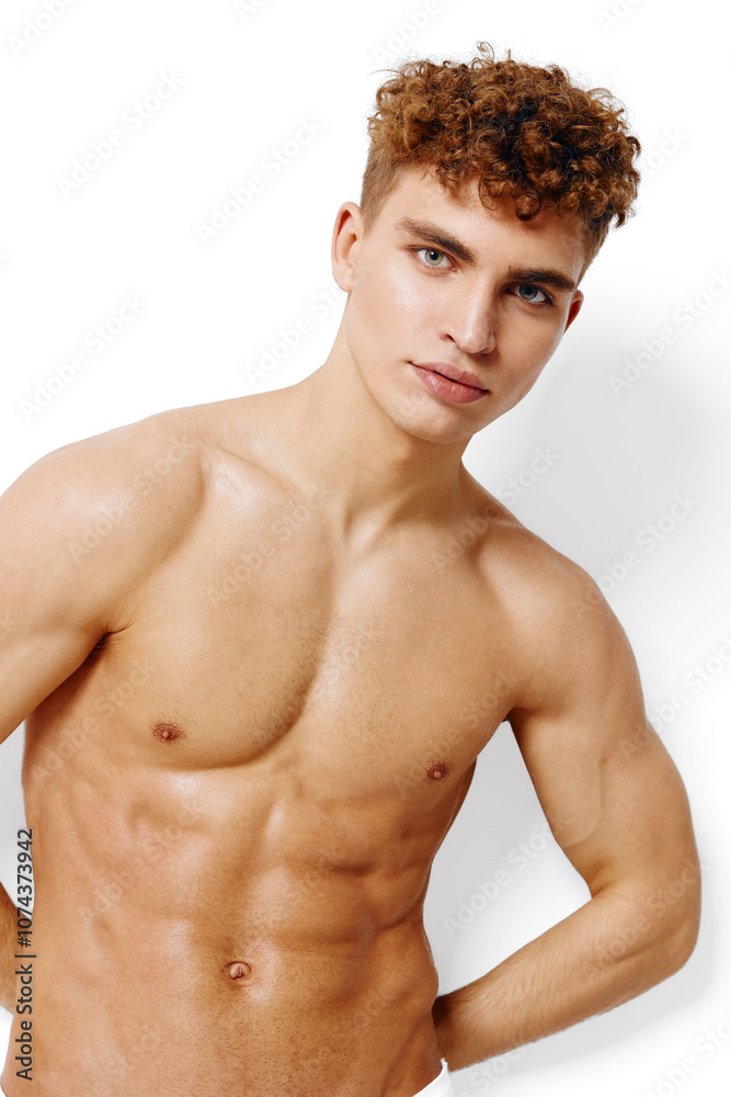 Fototapeta premium Confident young man with curly hair posing shirtless against a white background, showcasing a fit physique and healthy lifestyle. Fitness and masculinity concept.