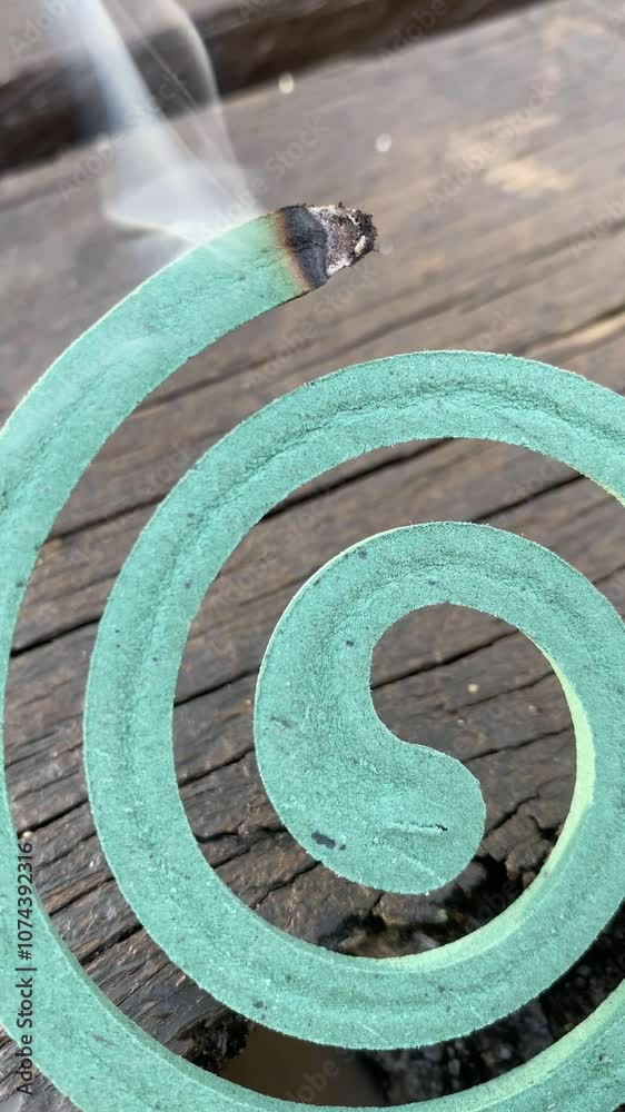 Burning mosquito coil releasing smoke on wooden surface outdoors