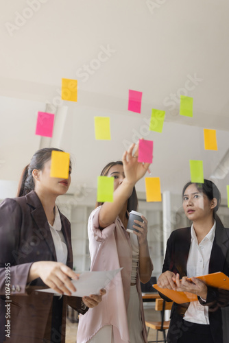 Asian businesswoman teamwork planning with sticky notes and new ideas on a glass wall, Business people brainstorming strategy and new ideas concept, startup worker meeting,