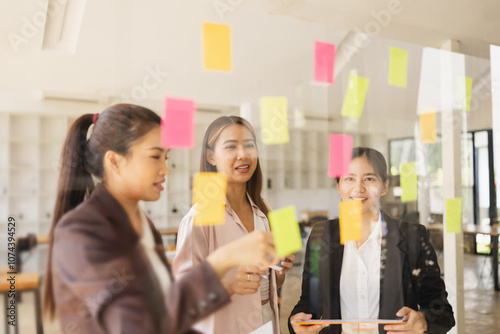 Asian businesswoman teamwork planning with sticky notes and new ideas on a glass wall, Business people brainstorming strategy and new ideas concept, startup worker meeting,