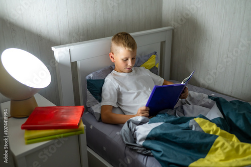 fair-haired teenage boy reading a book before bed photo