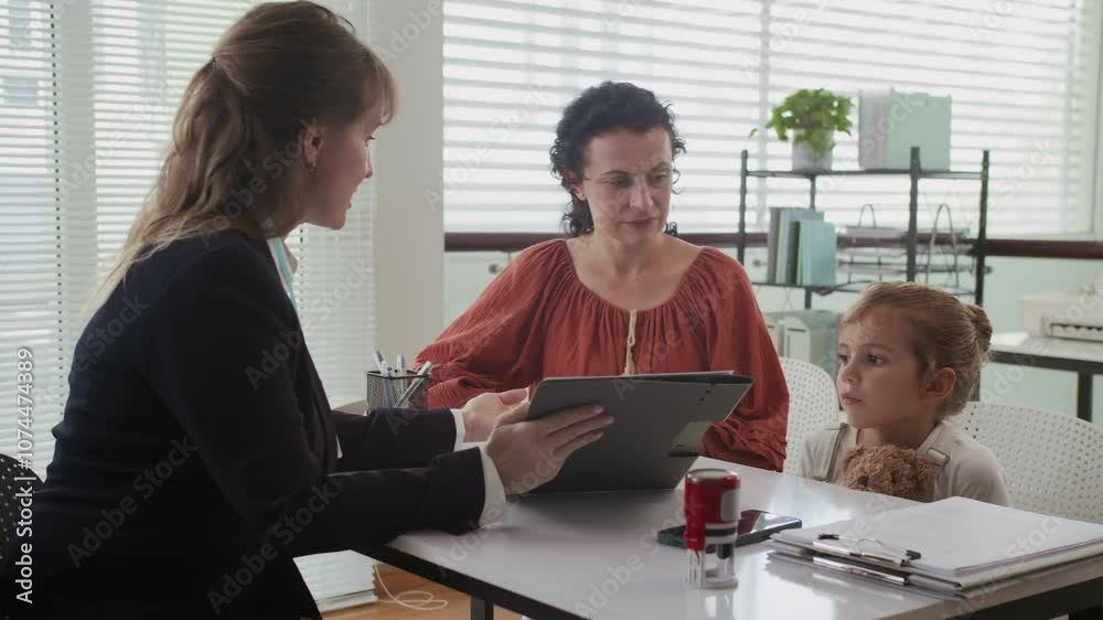 Medium shot of female middle-aged consultant talking to mother visiting social office with daughter Medium shot of female middle-aged consultant talking to mother visiting social office with daughter