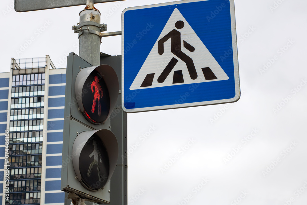 There is a pedestrian crossing sign positioned next to a traffic light There is a pedestrian crossing sign positioned next to a traffic light