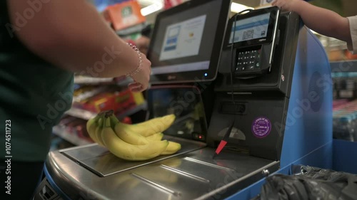 person scans bananas at self-checkout station in grocery store, with screen and payment terminal in view, reflecting modern shopping experience. scans bananas at self-checkout station, grocery store