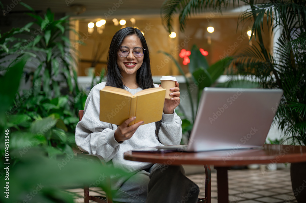 A beautiful, relaxed Asian woman in a cozy sweater enjoys coffee while reading at an outdoor table. A beautiful, relaxed Asian woman in a cozy sweater enjoys coffee while reading at an outdoor table.