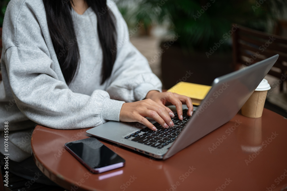Naklejka premium A close-up of an Asian woman working on her laptop at an outdoor table of a coffee shop.