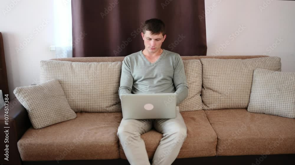 Focused man sitting on sofa in apartment with laptop and working online. Freelancer working from home, online work. Student learning online. Focused man sitting on sofa in apartment with laptop and working online. Freelancer working from home, online work. Student learning online.