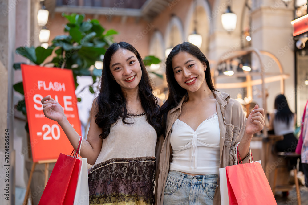 Two attractive Asian women standing in a shopping mall with a flash sale sign in the background. Two attractive Asian women standing in a shopping mall with a flash sale sign in the background.