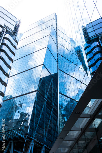 The glass facade of a skyscraper beautifully reflects its surroundings, creating a glistening effect under the sun, showing urban innovation and vertical expansion in London UK