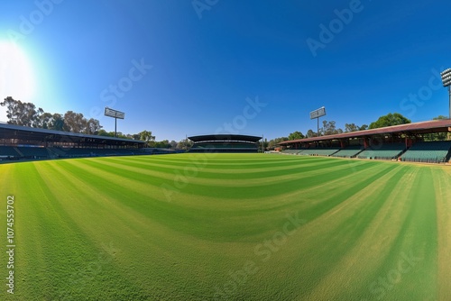 Cricket ground panoramic view, lush green grass, clear blue sky, stadium seating