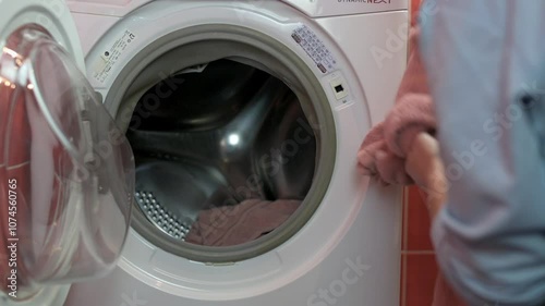Close-up of person loading pink towel into front-loading washing machine, emphasizing laundry day chores and household activities. person loading into washing machine, loading into washing machine