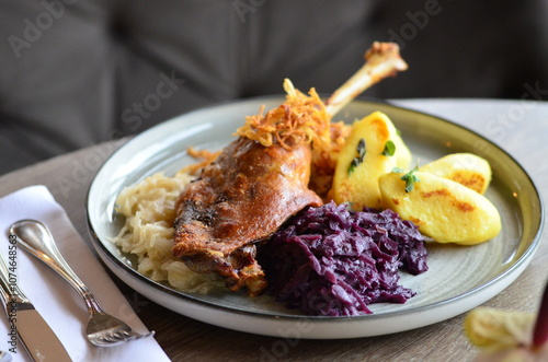 close view of roasted goose legs, red and white cabbage, potato dumplings, served food on a plate in a restaurant, wooden table, St. Martin's goose, traditional Czech holiday food photo