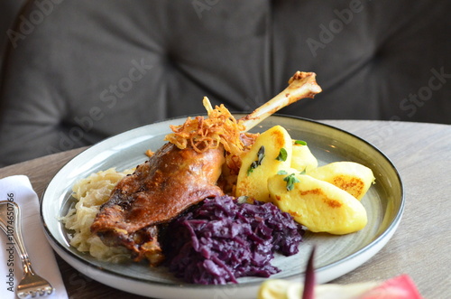 close view of roasted goose legs, red and white cabbage, potato dumplings, served food on a plate in a restaurant, wooden table, St. Martin's goose, traditional Czech holiday food photo