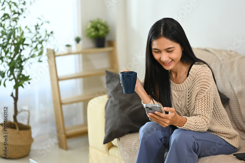 Cheerful young woman holding a coffee cup and reading messages on smartphone