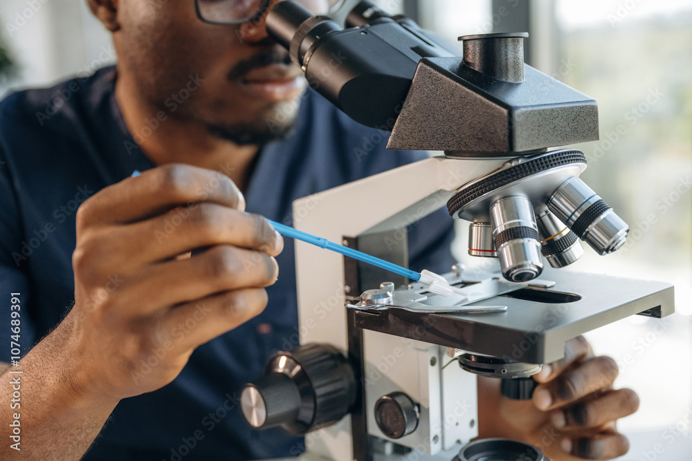 Focused on job. Scientist is working indoors, microscope is on the table Focused on job. Scientist is working indoors, microscope is on the table