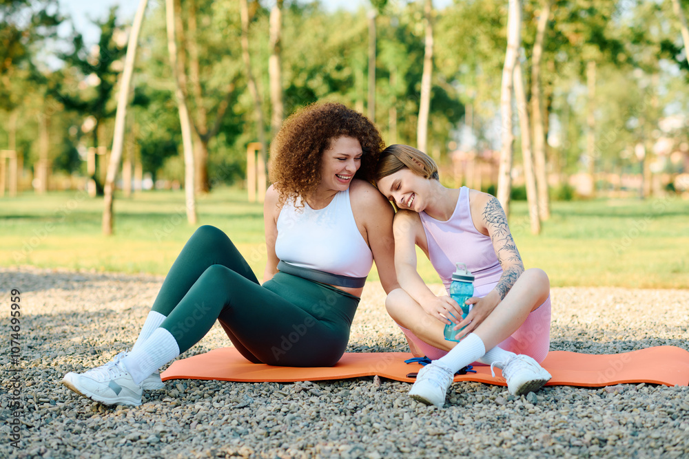 Two women share laughter and affection while sitting on yoga mats in the park. Two women share laughter and affection while sitting on yoga mats in the park.
