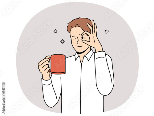 Sleepy man with mug of coffee, opens eyes with hand and needs to rest due to lack of energy and drowsiness. Tired young guy drinks coffee drink to cheer up and continue productive work.