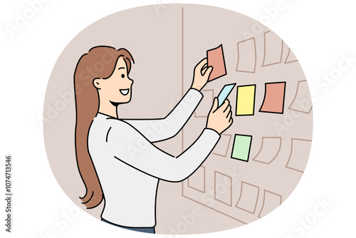 Business woman stands near scrum board with stickers and is engaged in kanban task planning. Girl manager or team leader of it company smiling while preparing new scrum sprint for programmers