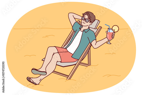 Man tourist is sunbathing on beach sitting in sun lounger and drinking fruity refreshing cocktail. Guy tourist and travel lover sunbathes spending vacation on beach of sunny ocean.