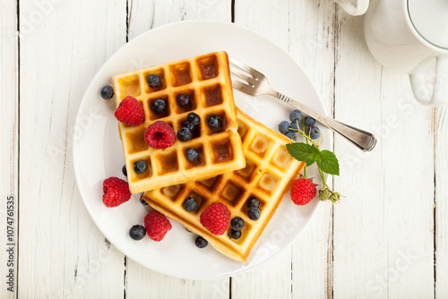 Handmade Belgian Waffles with blueberries and raspberries on plate, on rustic wooden table