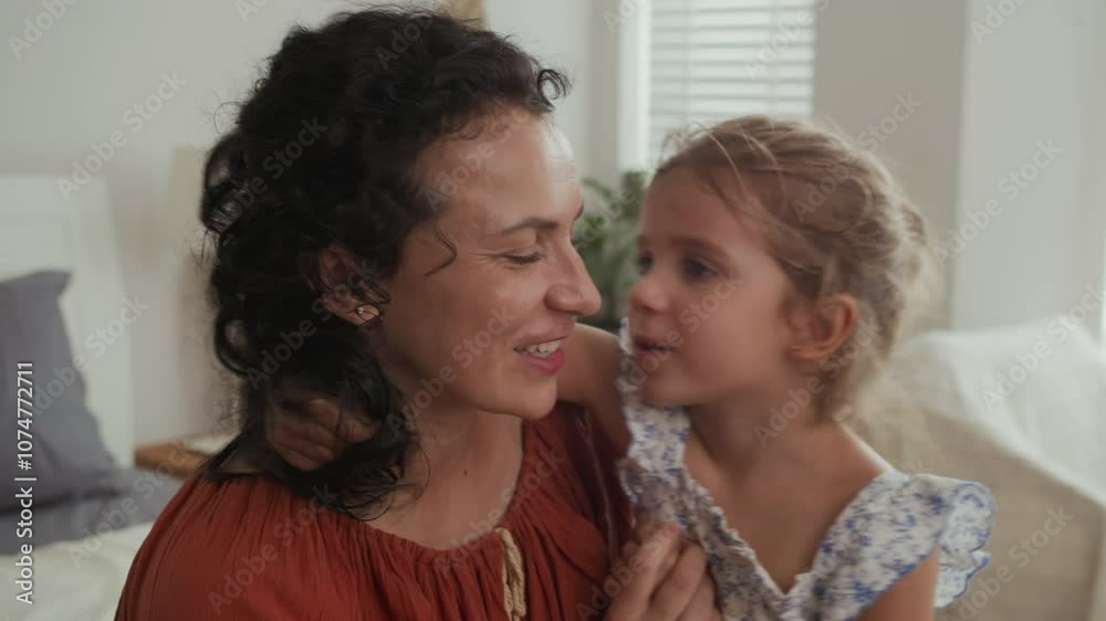 Medium close up of cute little girl kissing her mother in cheek while spending time together at home