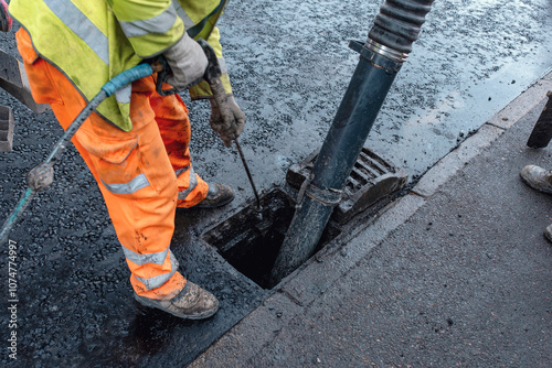 Construction worker operates a vacuum truck to clear debris from a storm drain on a busy city street during the day photo