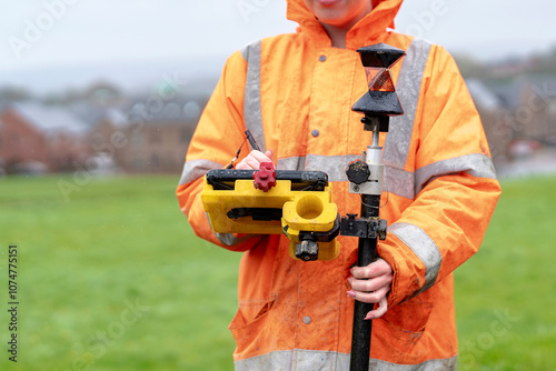 Bilde på lerret Surveyor in bright orange rain gear measures land using surveying tools on a clo